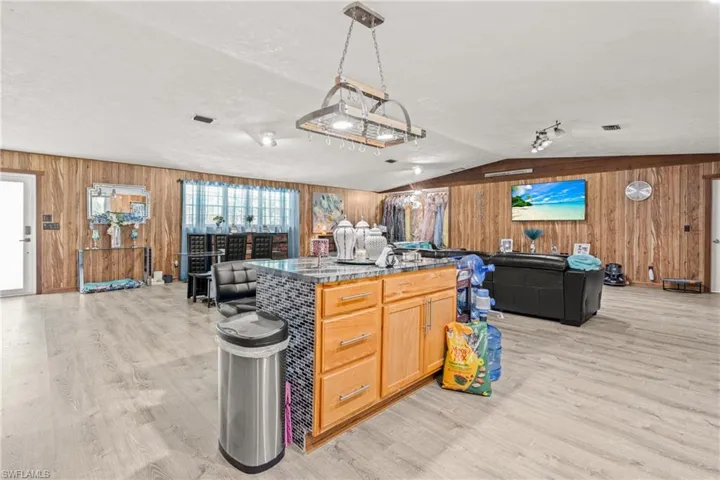 Kitchen with wood walls, open floor plan, light wood finished floors, dark countertops, and a kitchen island