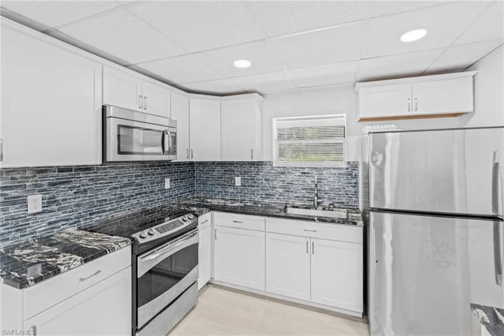 Kitchen with stainless steel appliances, white cabinetry, decorative backsplash, a drop ceiling, and recessed lighting