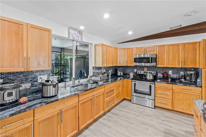 Kitchen featuring dark stone countertops, appliances with stainless steel finishes, backsplash, lofted ceiling, and light wood-style floors