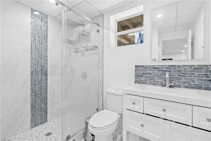 Full bath featuring a paneled ceiling, backsplash, vanity, and a marble finish shower