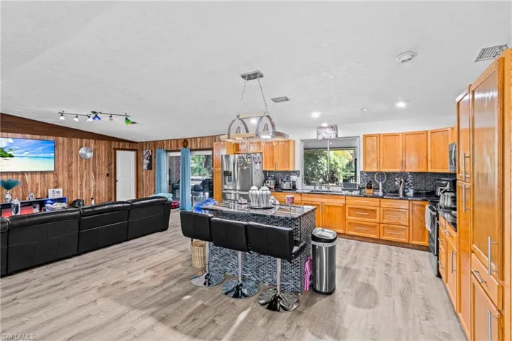 Kitchen with open floor plan, wood walls, pendant lighting, light wood-style flooring, and appliances with stainless steel finishes
