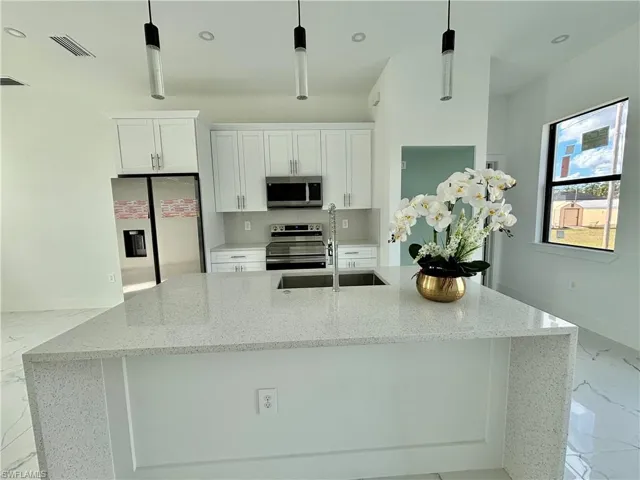 Kitchen featuring light stone counters, white cabinetry, appliances with stainless steel finishes, and pendant lighting