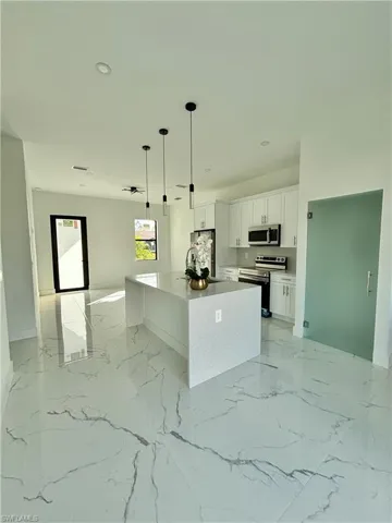 Kitchen featuring sink, decorative light fixtures, an island with sink, stainless steel appliances, and white cabinets