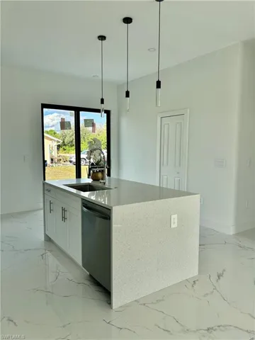 Kitchen featuring sink, an island with sink, white cabinets, decorative light fixtures, and stainless steel dishwasher