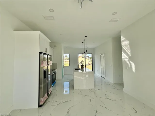 Kitchen with white cabinetry, stainless steel fridge, a kitchen island with sink, and pendant lighting