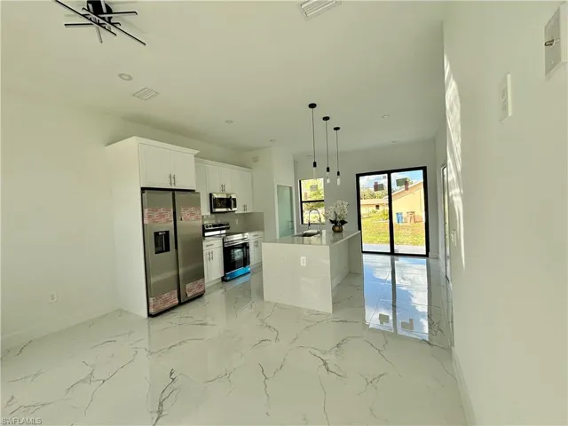 Kitchen with appliances with stainless steel finishes, decorative light fixtures, white cabinetry, an island with sink, and sink