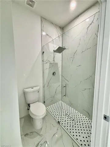 Bathroom featuring a shower with door and toilet