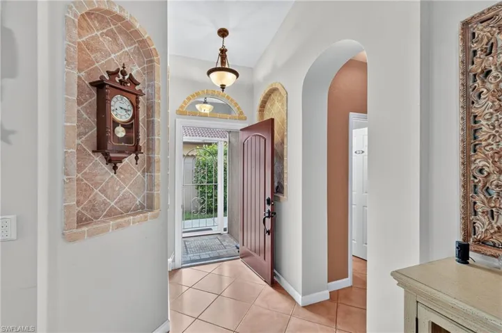 Arched entryways, tile flooring, built-in wall niche with stone-tile detailing, and a dark wood-finish front door