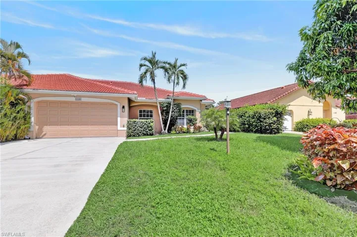 Exterior featuring a terracotta tile roof, attached garage, concrete driveway, and established landscaping