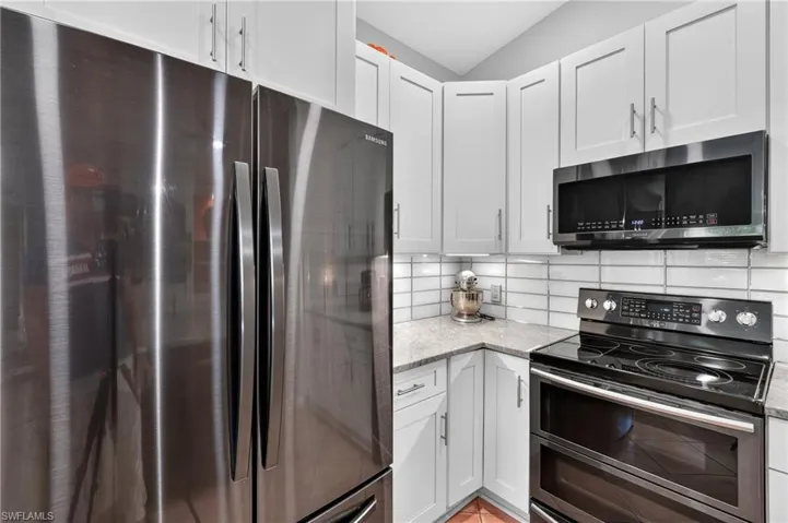 Stainless steel refrigerator, white shaker-style cabinetry, light granite countertops, white subway tile backsplash, and black stainless steel range with microwave