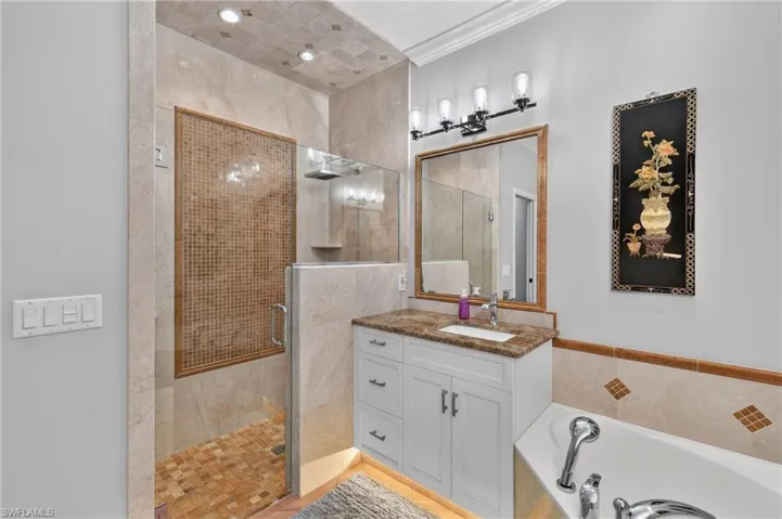 Walk-in shower with glass enclosure and mosaic tile, single vanity with countertop, framed mirror, and built-in bathtub