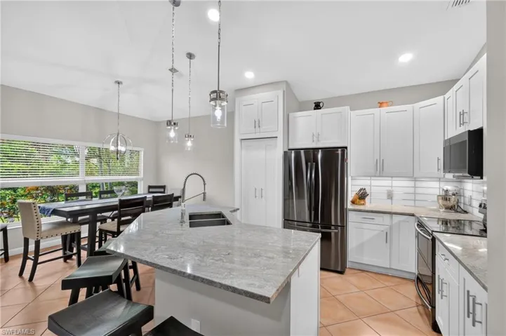 Kitchen featuring an island with a sink, pendant lighting, white cabinetry, integrated stainless-steel appliances, and tile flooring