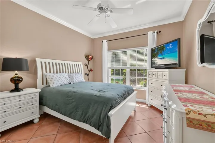 Bedroom 1 - Terracotta-style tile flooring, white crown molding, ceiling fan with light fixture, window with horizontal blinds, and ample natural light