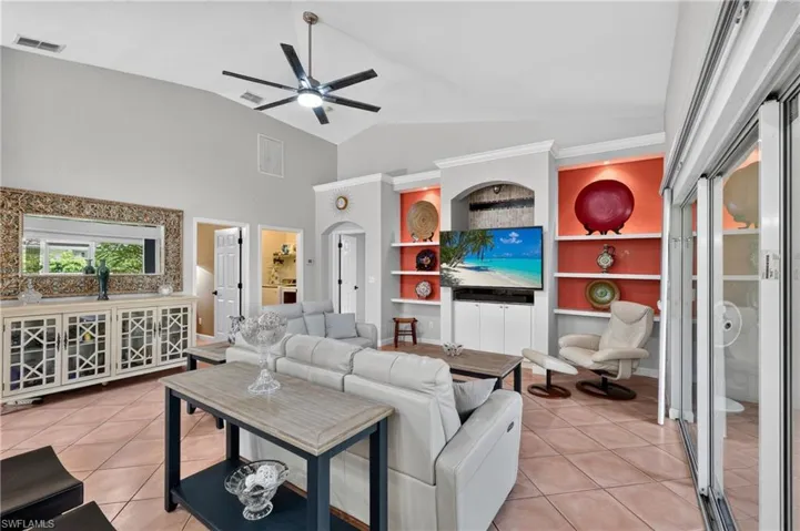 Vaulted ceilings with a ceiling fan, built-in shelving with accent lighting, tile flooring, and large sliding glass doors