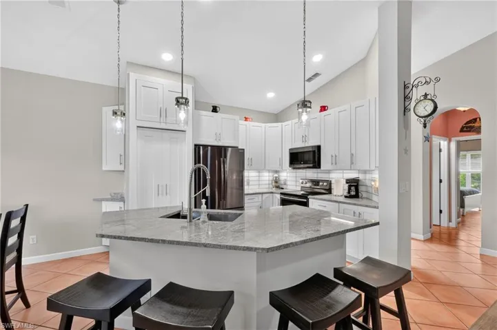 Kitchen featuring white shaker-style cabinetry, a large kitchen island with a stone-finish countertop, a stainless steel sink with a gooseneck faucet, and pendant lighting