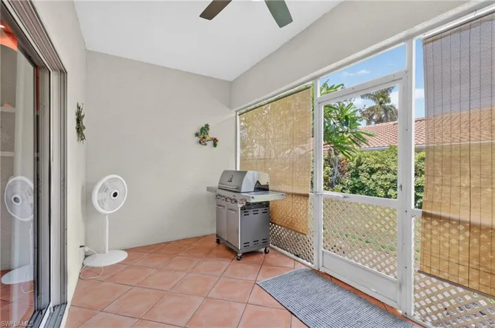 Screened-in patio with terracotta tile flooring, sliding glass door access, and a ceiling fan