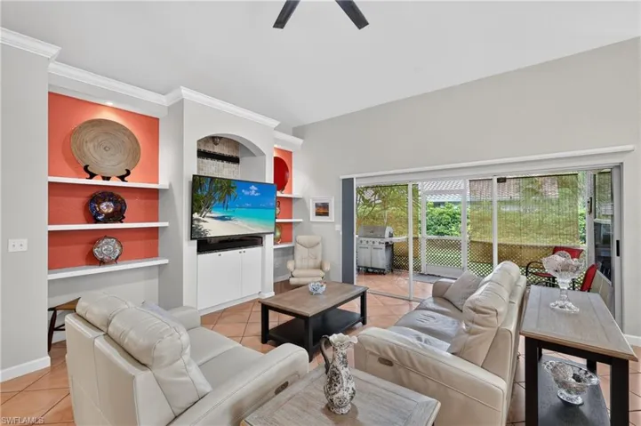 Built-in shelving with accent wall, arched alcove, integrated media console, ceiling fan, and sliding glass doors to outdoor patio