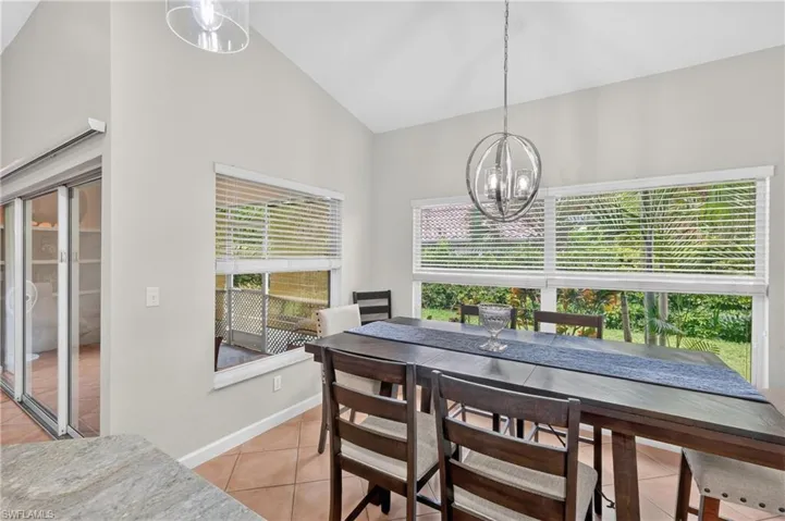 Vaulted ceiling with an orb chandelier, large windows with horizontal blinds, terracotta-style flooring, and a sliding glass door