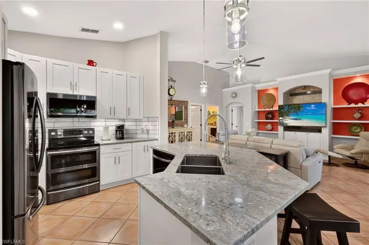 Open-concept kitchen featuring white cabinetry, stainless steel appliances, and a large central island with an integrated sink and breakfast bar