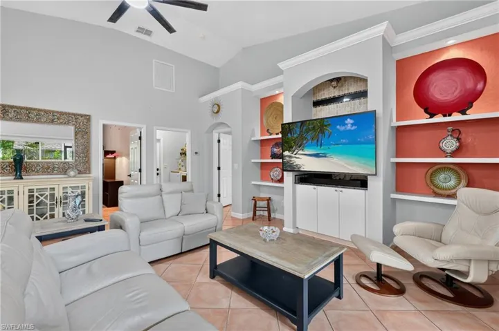 Living area featuring vaulted ceilings, ceiling fan, tile flooring, and custom built-ins with integrated shelving