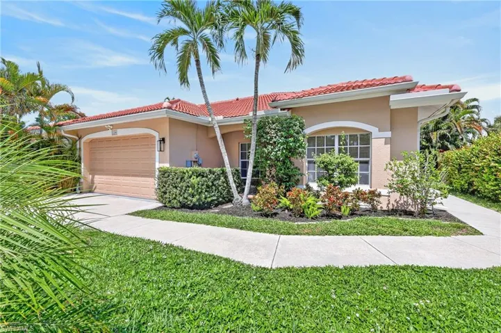 Stucco exterior with a terracotta tile roof, arched garage door, arched window, and established landscaping