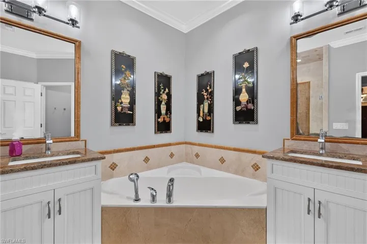 Dual vanities with granite countertops, built-in corner bathtub, and tiled surround
