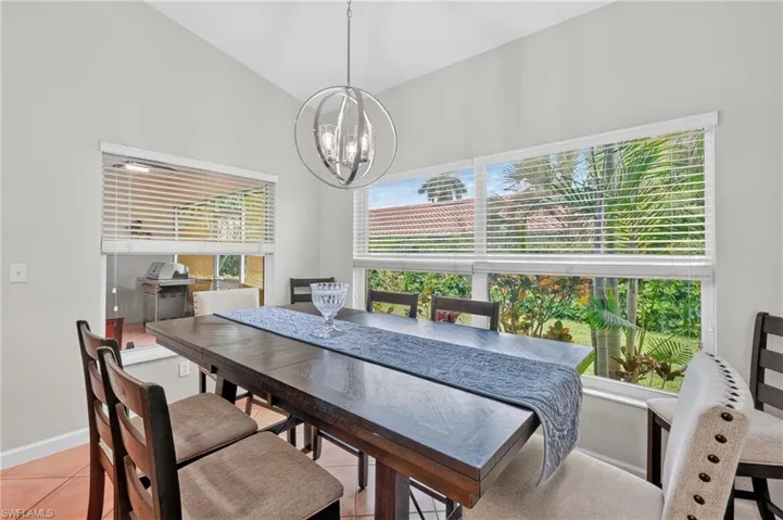 Vaulted ceiling with a contemporary chandelier, two large windows, light neutral wall paint, and tiled flooring