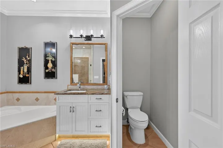 Guest Bathroom -Built-in corner soaking tub with tiled surround, white vanity with stone countertop, undermount sink, and wall-mounted light fixture, and a separate toilet enclosure