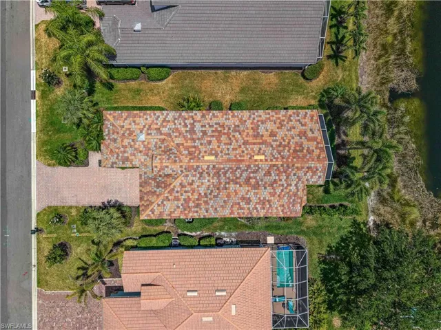 Aerial view of a property featuring a multi-toned tile roof, green lawn, and mature palm trees