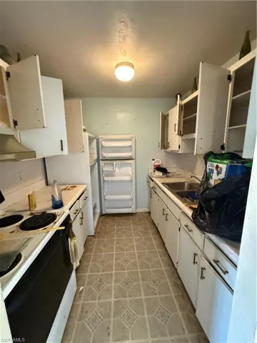Kitchen featuring range, light tile patterned flooring, white cabinets, exhaust hood, and sink