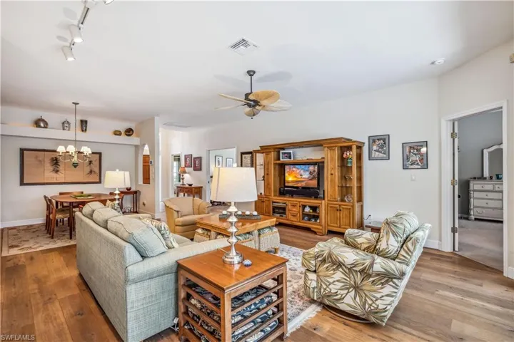 Living room with light hardwood flooring, ceiling fan with chandelier, and track lighting