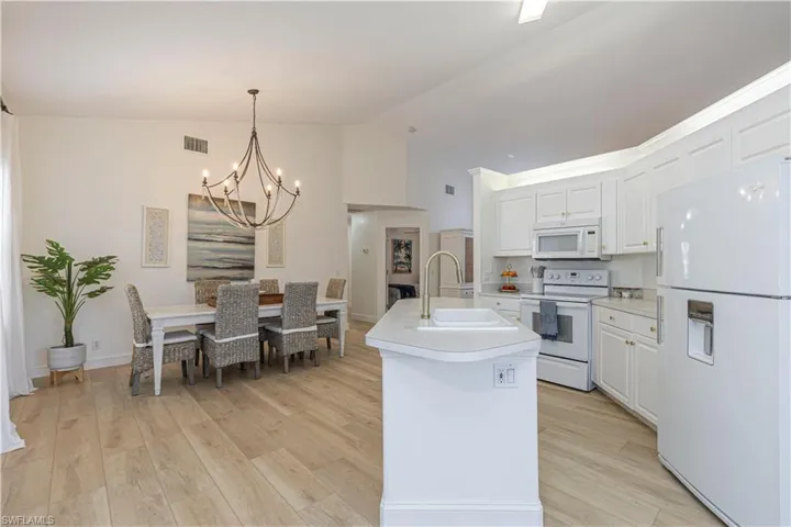 Kitchen with white cabinetry, white appliances, a kitchen island with sink