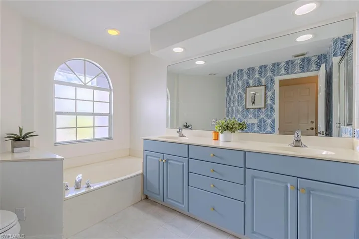 Master Bathroom with double sinks, tile patterned floors, toilet, and a bathing tub