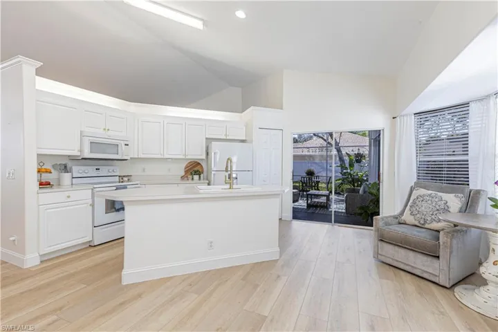 Kitchen featuring vaulted ceiling, white cabinetry, an island with sink, white appliances, and light wood-type flooring
