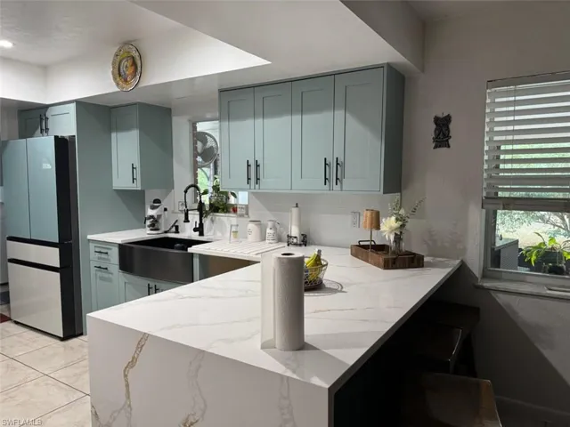 Kitchen featuring a peninsula, light stone countertops, freestanding refrigerator, decorative backsplash, and a kitchen bar