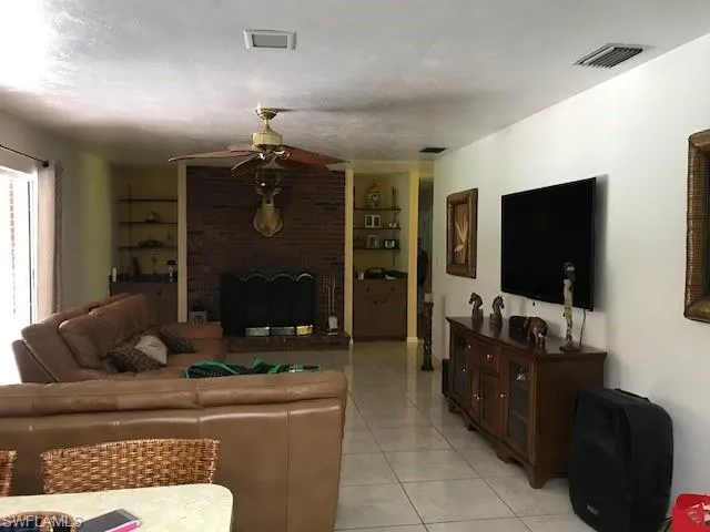 Living area with a brick fireplace, ceiling fan, built in shelves, light tile patterned flooring, and a textured ceiling