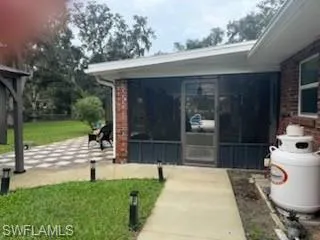 Property entrance with a sunroom, brick siding, and a lawn