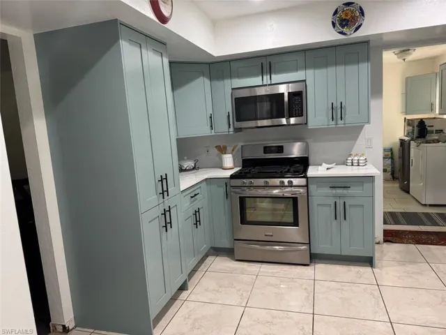 Kitchen featuring appliances with stainless steel finishes, light stone countertops, washer and clothes dryer, and green cabinetry