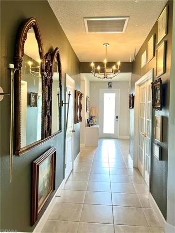 Entryway with a chandelier, light tile patterned flooring, a textured ceiling, french doors, and baseboards.