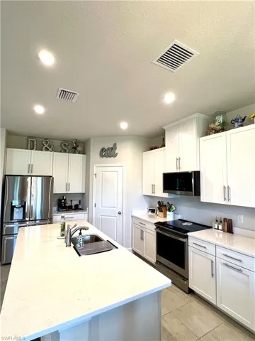 Kitchen with appliances with stainless steel finishes, a sink, recessed lighting, white cabinetry, and a textured ceiling