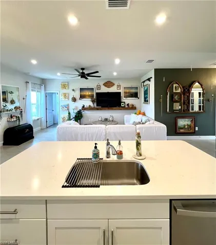 Kitchen with open floor plan, a sink, stainless steel dishwasher, white cabinets, and ceiling fan
