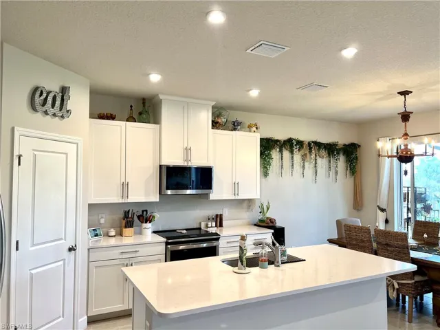 Kitchen featuring appliances with stainless steel finishes, a sink, light countertops, white cabinetry, and a chandelier