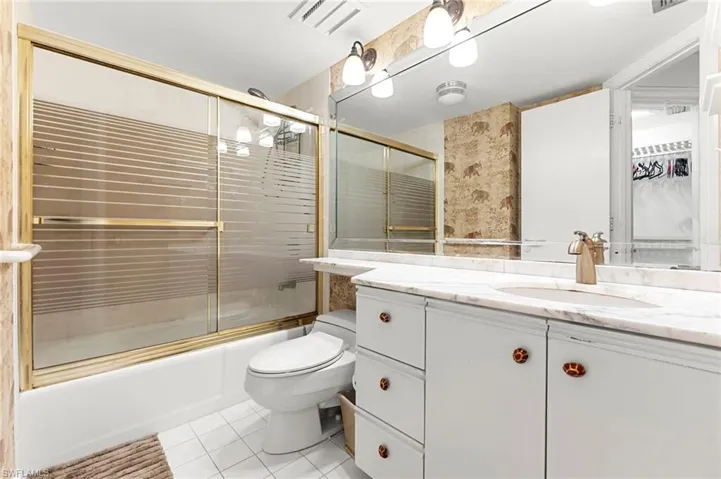 Bathroom with vanity, enclosed tub / shower combo, light tile patterned floors, and a walk in closet