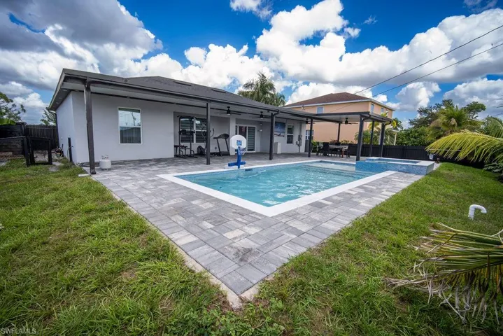 Rear view of house with a fenced backyard, a ceiling fan, a patio, and a pool with connected hot tub