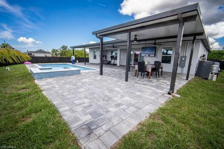 Fenced backyard with a patio area, ceiling fan, a pool with connected hot tub, and outdoor dining area