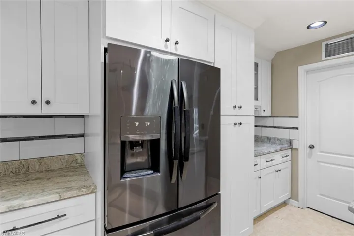 Kitchen with white cabinetry, light tile flooring, stainless steel fridge with ice dispenser, and light stone countertops