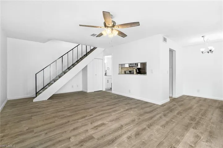 Unfurnished living room featuring wood-type flooring and ceiling fan with notable chandelier