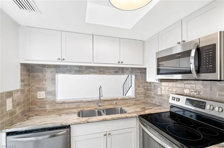 Kitchen with light stone countertops, backsplash, stainless steel appliances, sink, and white cabinets