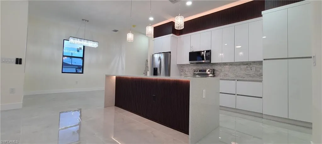 Kitchen with tasteful backsplash, stainless steel appliances, decorative light fixtures, a center island, and white cabinetry