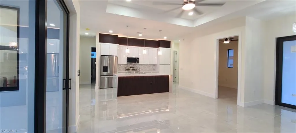 Kitchen with pendant lighting, a kitchen island with sink, stainless steel appliances, white cabinets, and a raised ceiling